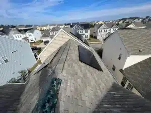 A rooftop view of a suburban neighborhood features rows of houses with varying shades of beige, gray, and white siding. Some roofs have solar panels installed, reflecting light like a halo. The sky is clear with a few scattered clouds, creating an idyllic backdrop for this scenic vista.